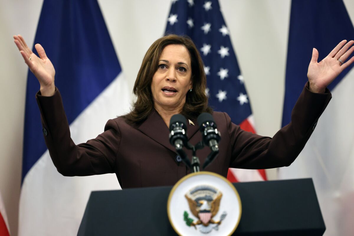 Vice President Kamala Harris holds her arms out while speaking behind a lectern