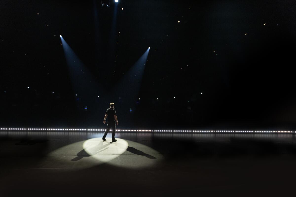 Ricky Gervais stands onstage with 2 spotlights shining down connected him