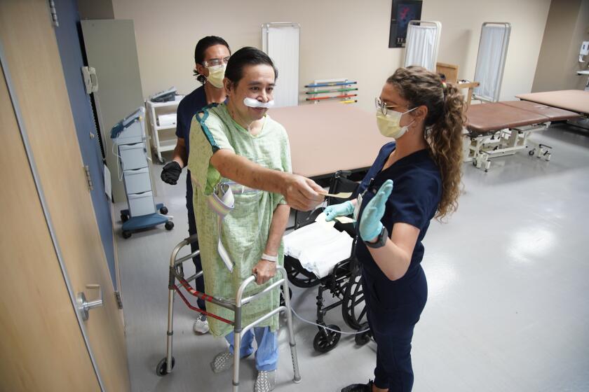 SAN DIEGO, CALIFORNIA - SEPTEMBER 29: On the left Philip Dicenso physical therapist helps Dr. Jay Buenaflor while Katherine Dailey occupational therapist receives paper note. The Brawley resident is currently rehabbing at Select Specialty Hospital on Tuesday, Sept. 29, 2020 in San Diego, California. (Alejandro Tamayo / The San Diego Union-Tribune)