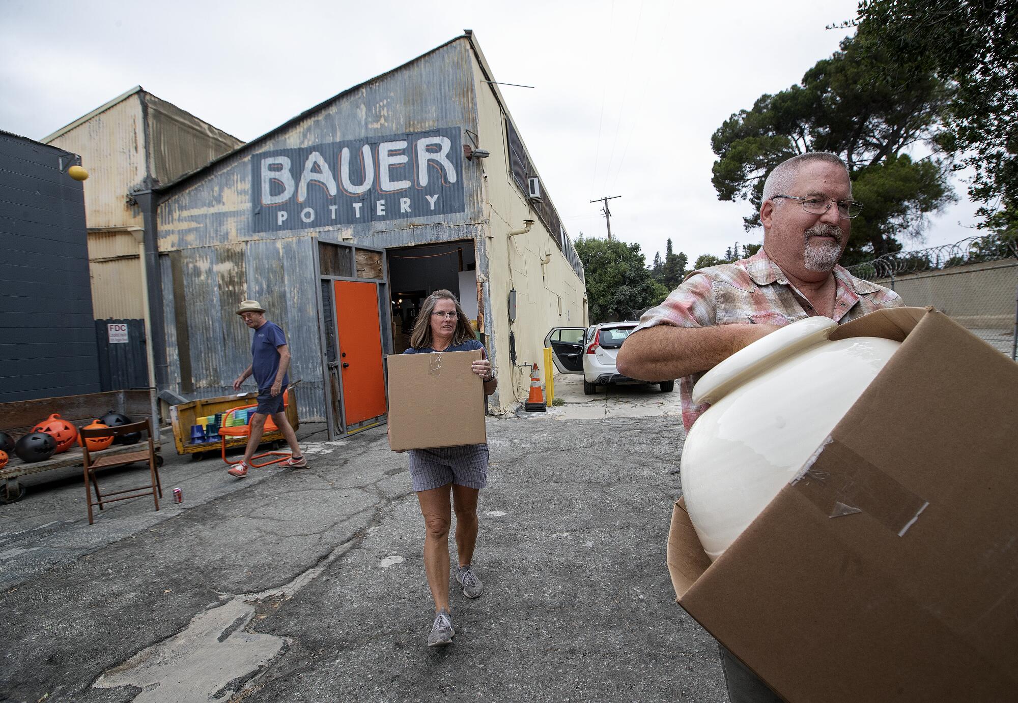 A man carries a large pot from an industrial building with a sign reading Bauer Pottery