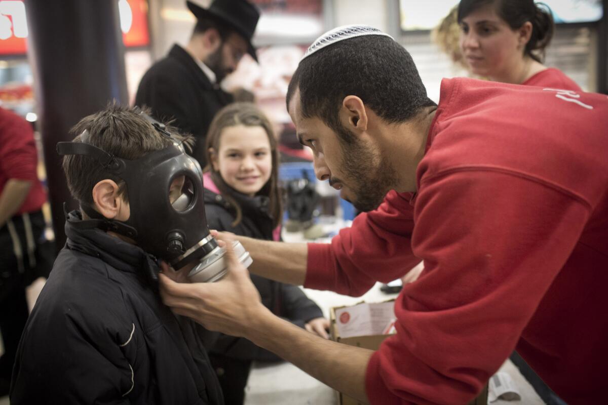 A post office worker shows an Israeli child how to wear a gas mask at a distribution station in a mall in East Jerusalem.