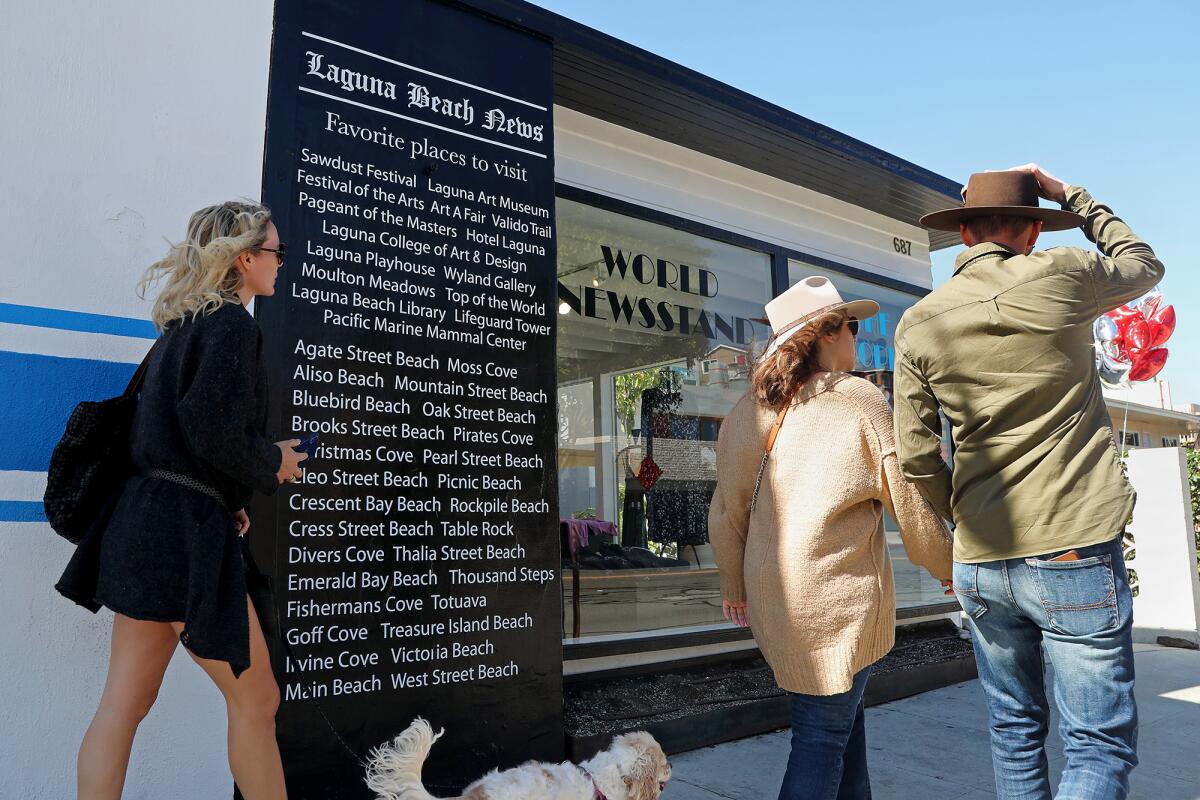 Pedestrians walk past the newspaper wall, designed by owner Heidi Miller, placed at the front entrance of World Newsstand.