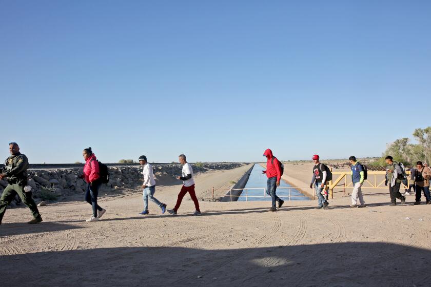 A border patrol agent leads asylum seekers to a van for transport along the Mexico/USA border, next to Cocopah Reservation land in Somerton, Arizona, on Thursday, May 4, 2023. Immigrants cross the border unimpeded and wait at this location for border patrol officers to take them to the Yuma Customs and Border Protection processing center.