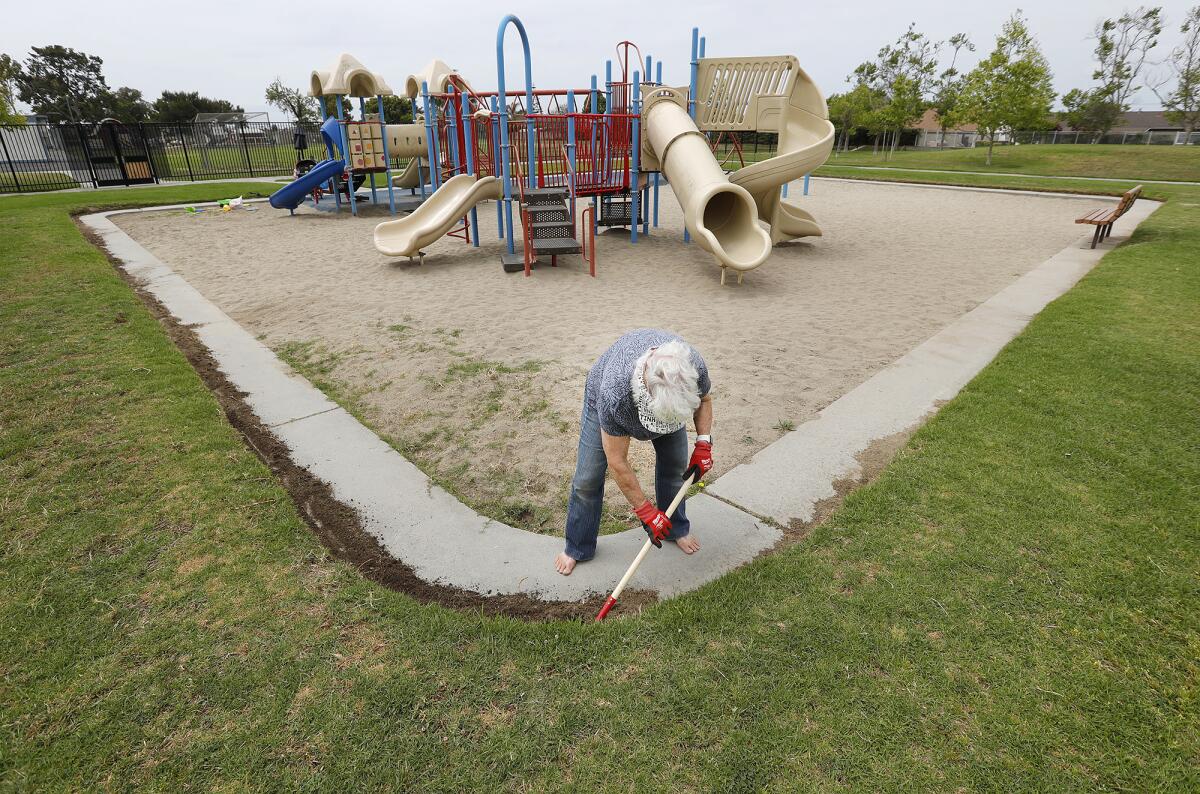 Maureen Farsadi clears overgrown grass from the path around the playground at Golden View Park in Huntington Beach on Monday.