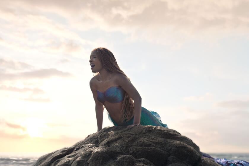 Halle Bailey sings while perched on a rock in the ocean a scene from "The Little Mermaid."