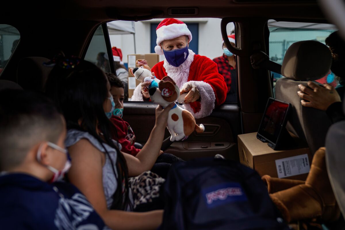 A man dressed as Santa hands gifts to students through a car window