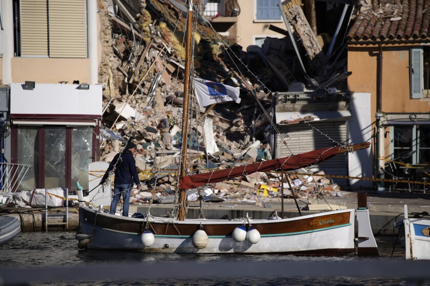 A resident moves a boat away from a fallen three-story apartment building after it collapsed in a suspected gas explosion on southern France's Mediterranean coast, Tuesday, Dec. 7, 2021 in Sanary-sur-Mer. French rescue workers dug out the body of a man but also pulled a toddler and the child's mother alive from the rubble of the building that collapsed in a suspected gas explosion. Two other people are missing. (AP Photo/Daniel Cole)