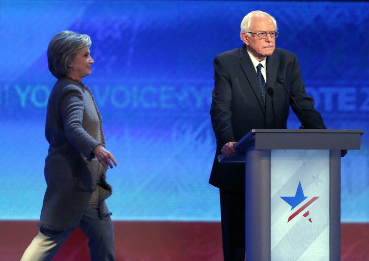 Hillary Clinton returns to the stage after the Democratic presidential primary debate had resumed from a break, as Bernie Sanders stands at his podium.