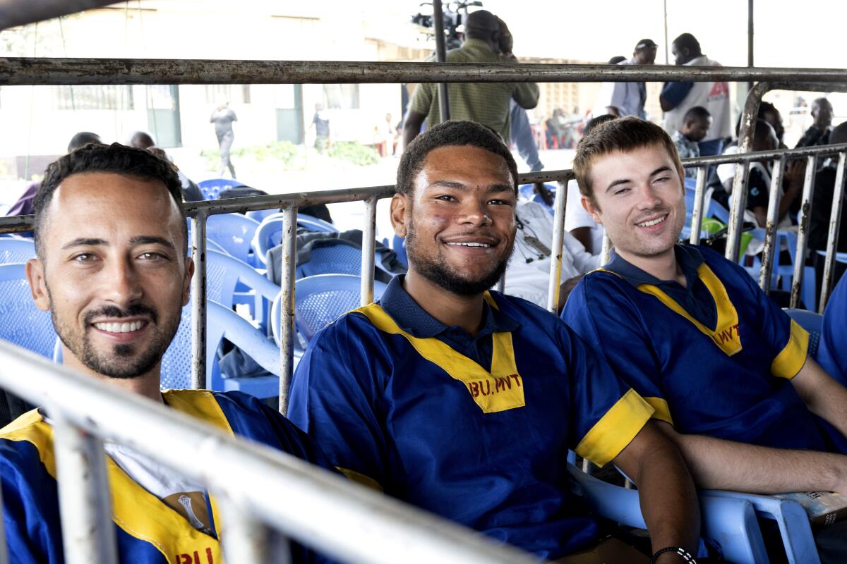 Three men in identical blue and yellow shirts smile.