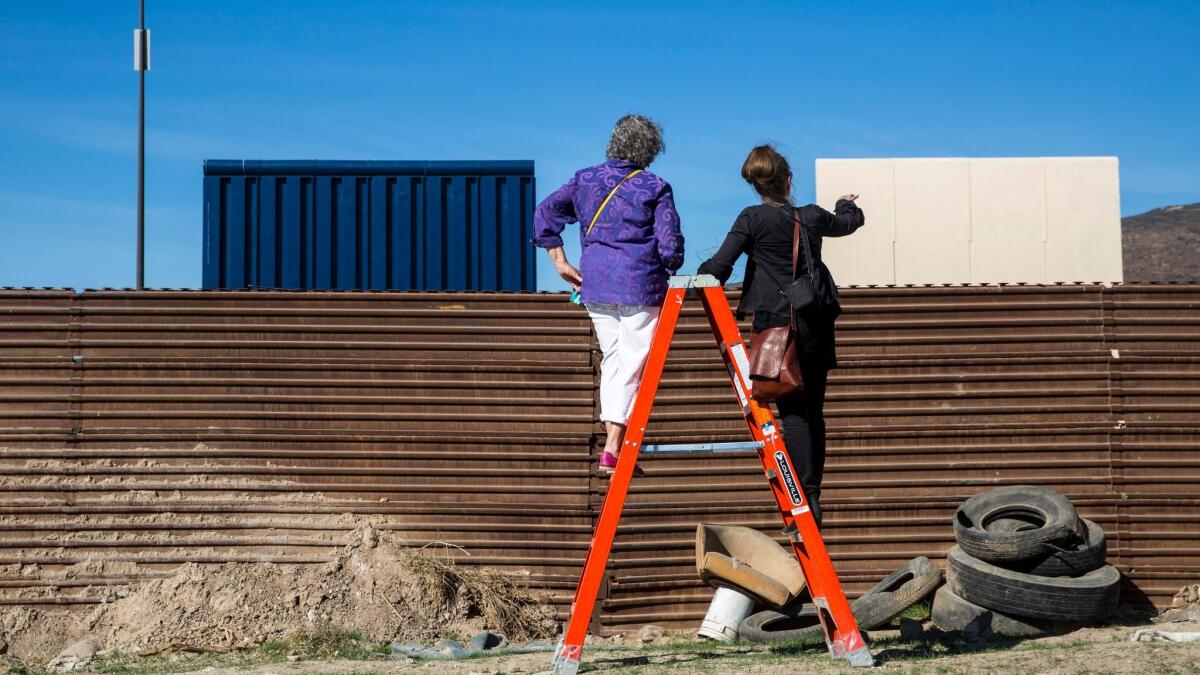 Participants on a tour of the border wall prototypes organized by artist Christoph Büchel peer at the structures from the Mexican side of the current border wall.