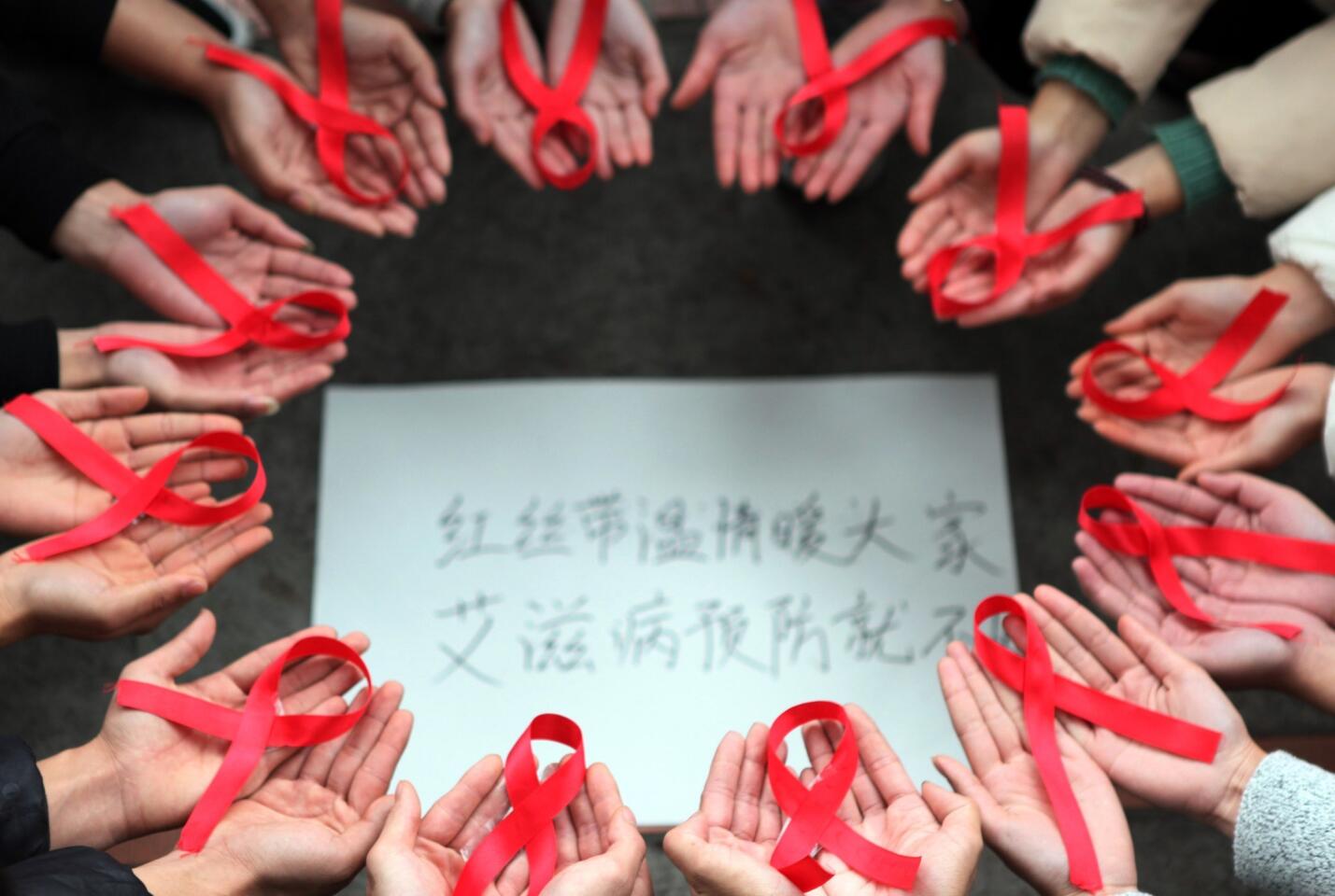 This picture taken on November 30, 2015 shows volunteers holding red ribbons above a piece of paper written in Chinese that reads ''Red ribbons bring warmth to everyone to prevent AIDS" during an event for World Aids Day in Chongqing.