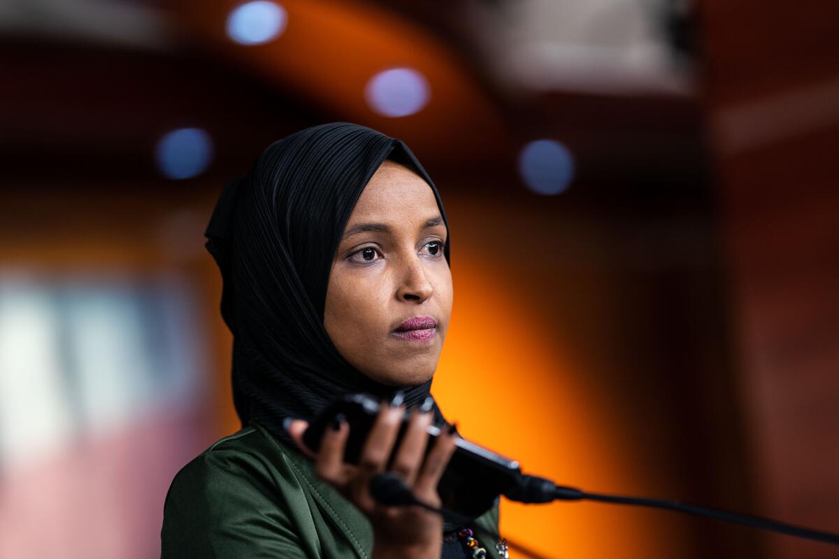 A woman with a dark head covering holds up a cellphone near microphones 