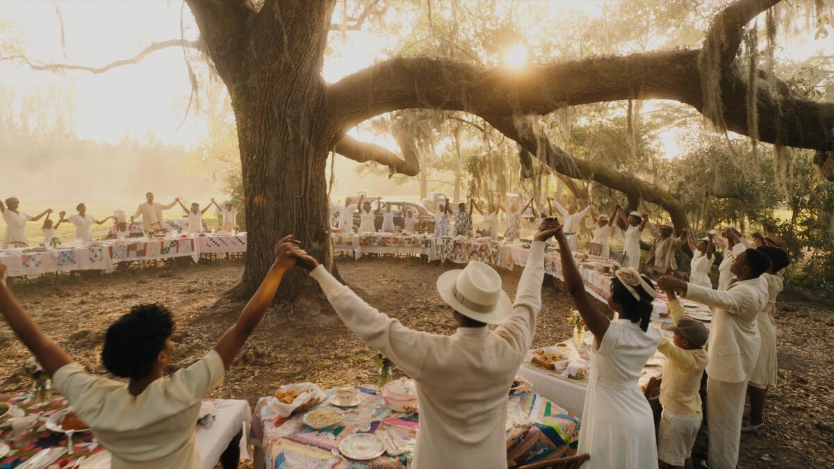 A ring of buffet tables encircles a large tree as guests join hands and lift them high in "The Color Purple." 
