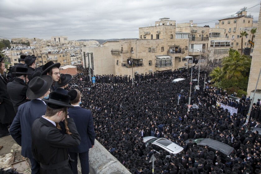 Men in ultra-Orthodox garb look down at a black-hatted sea of people surrounding several cars.