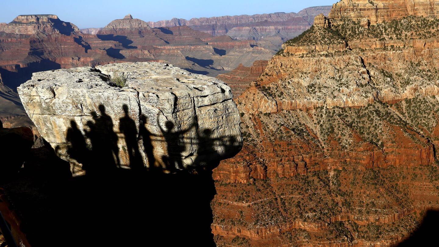 Visitors cast their shadows on a boulder while photographing the Grand Canyon from Mather Point.