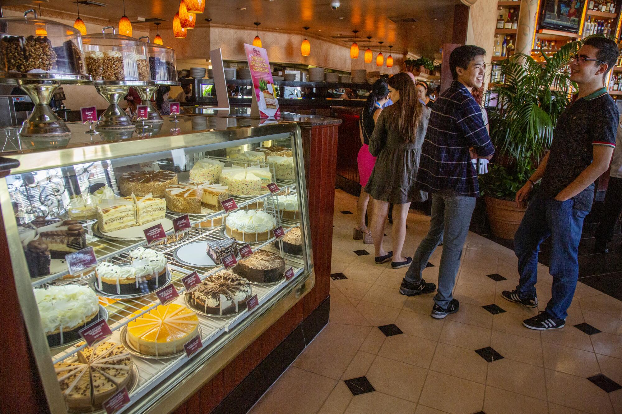 Customers by the cheesecake display waiting to be seated at a Cheesecake Factory restaurant.