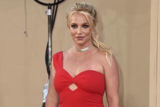 Britney Spears poses in a red dress against a gold background.