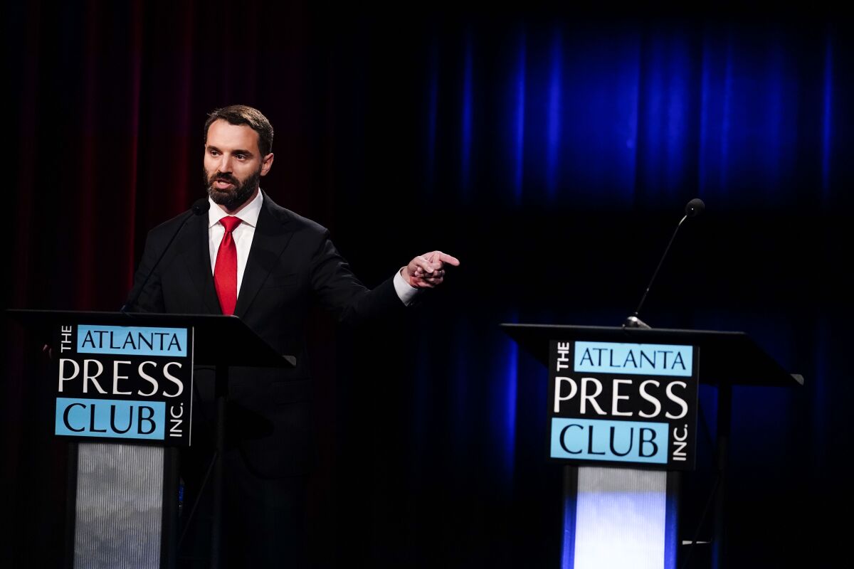 Georgia U.S. Senate candidate Latham Saddler points at an empty podium belonging to candidate Herschel Walker as he participates in a Republican primary debate on Tuesday, May 3, 2022, in Atlanta. (AP Photo/Brynn Anderson, Pool)