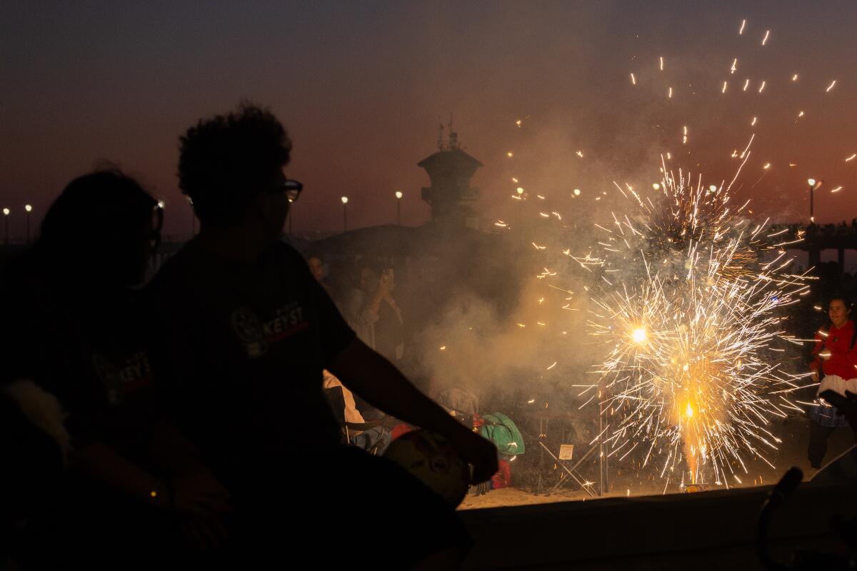 People watch fireworks explode at dusk near the pier at Huntington Beach. 