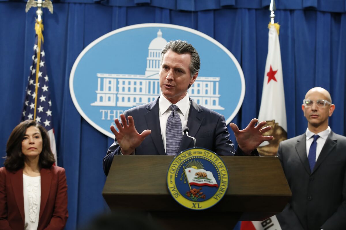 Gavin Newsom speaks at a press conference at a lectern with the seal of California
