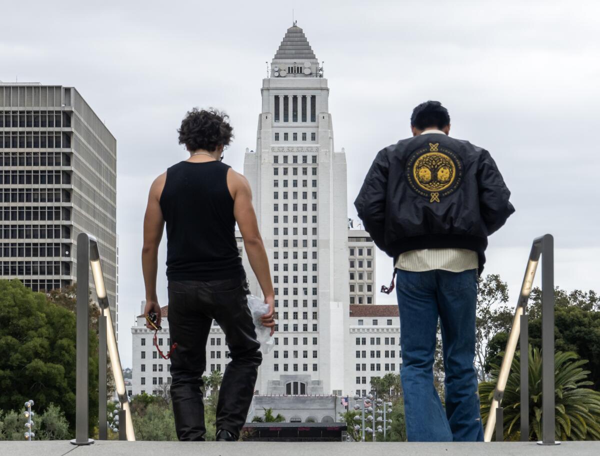 Two people walk with their backs to the camera, with Los Angeles City Hall in the background