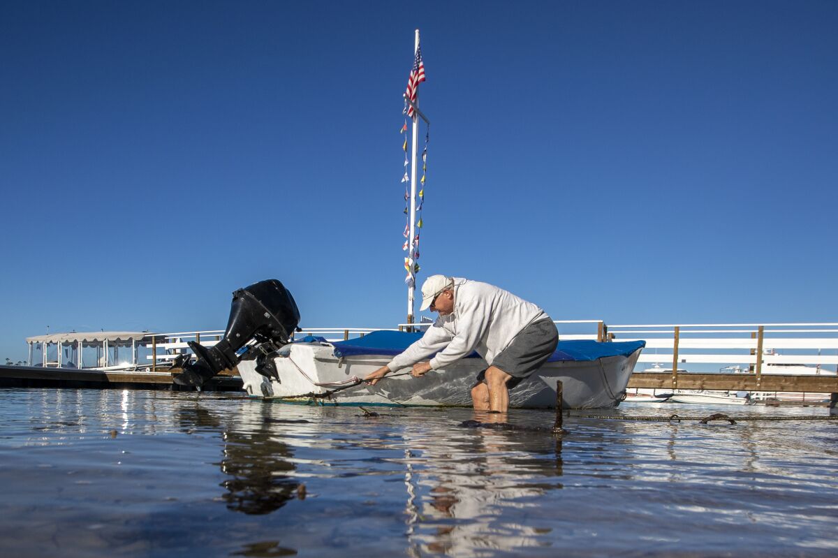 John Doughty unties a small boat as he wades into a king tide at Balboa Island.