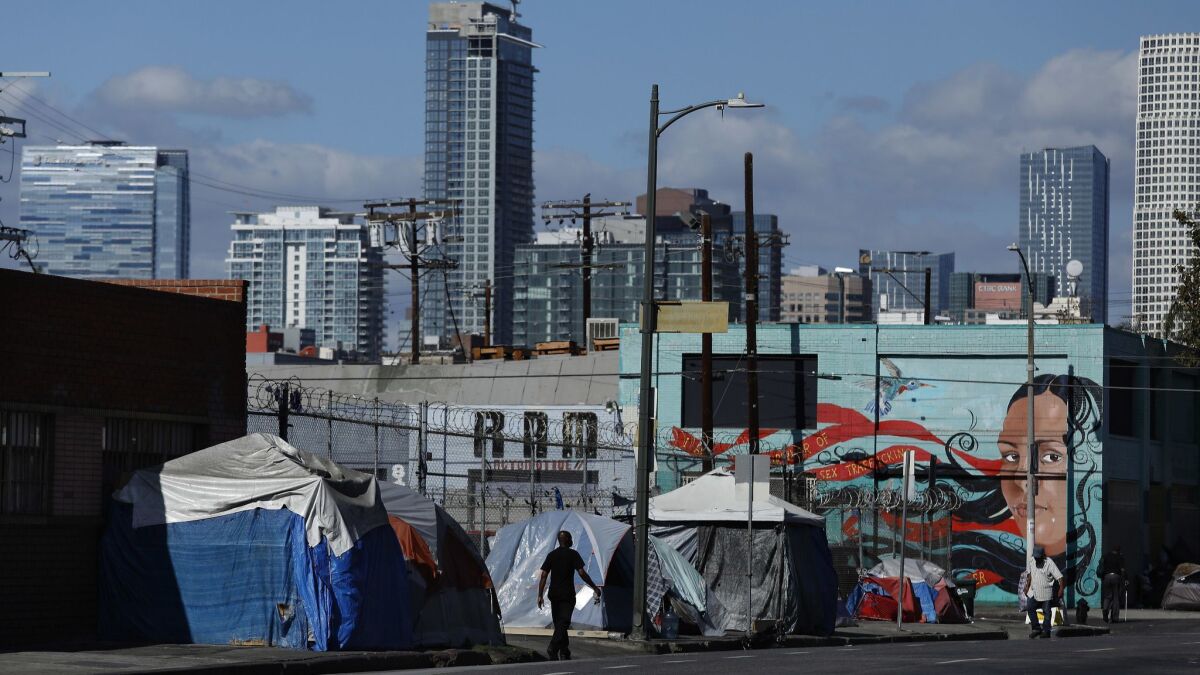 People walk past a homeless encampment on 6th St., just west of Central Ave. in downtown Los Angeles.