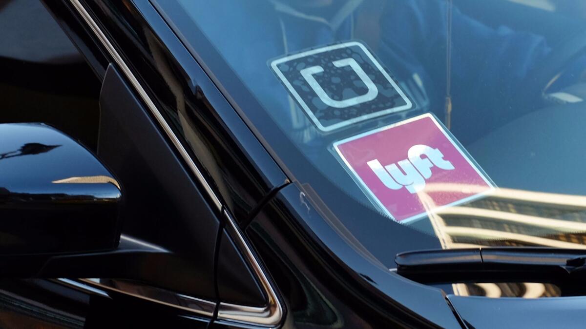 A driver displaying Uber and Lyft stickers on his front windshield drops off a customer in downtown Los Angeles. Half of corporate travel policies now allow business travelers to use such ride-sharing services, according to a new survey.
