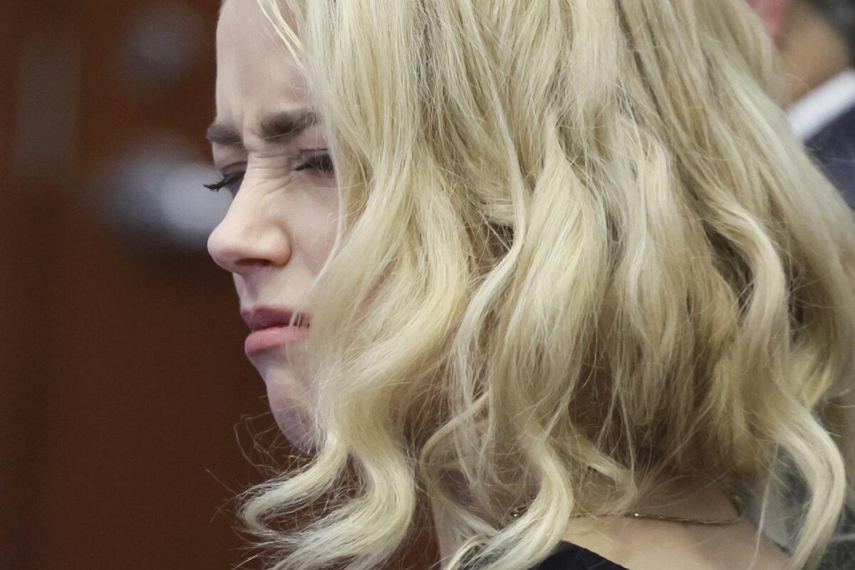 A woman with long, curly blond hair is shown in close-up squeezing her eyes shut in a pained expression