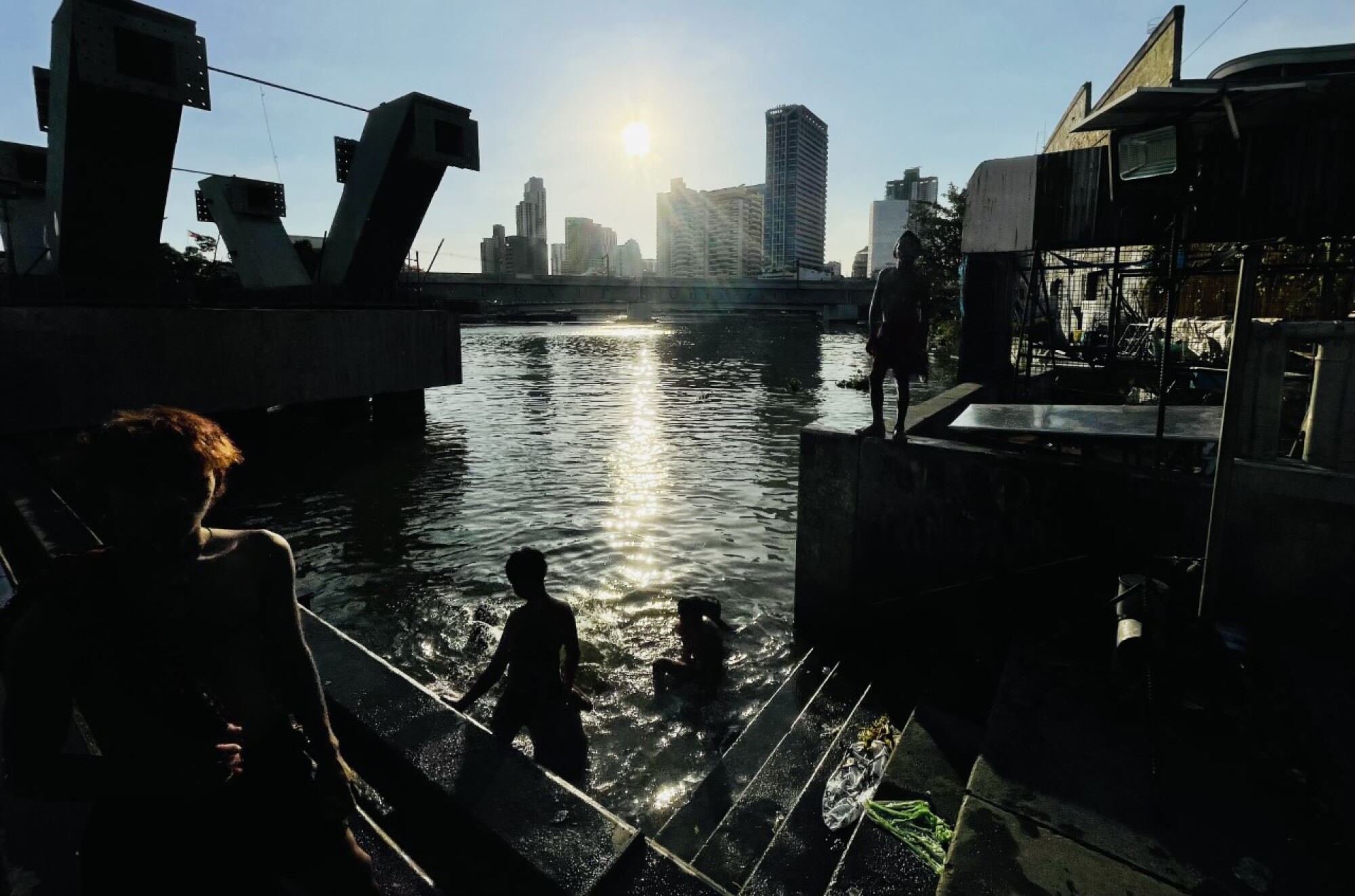 Kids swim in the Pasig River as the sun shines in the background