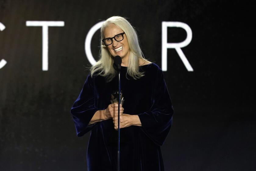 Jane Campion holding a trophy and smiling into a microphone