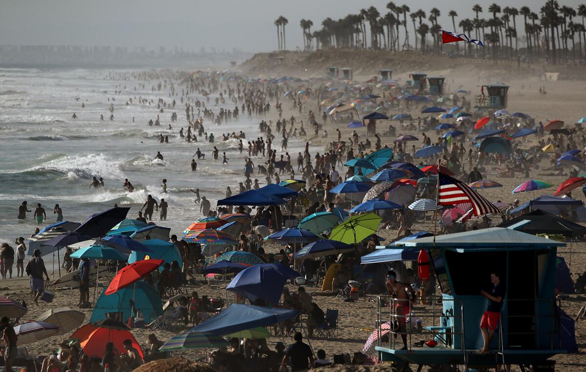 A shoreline is packed with swimmers and people on the sand beneath umbrellas.