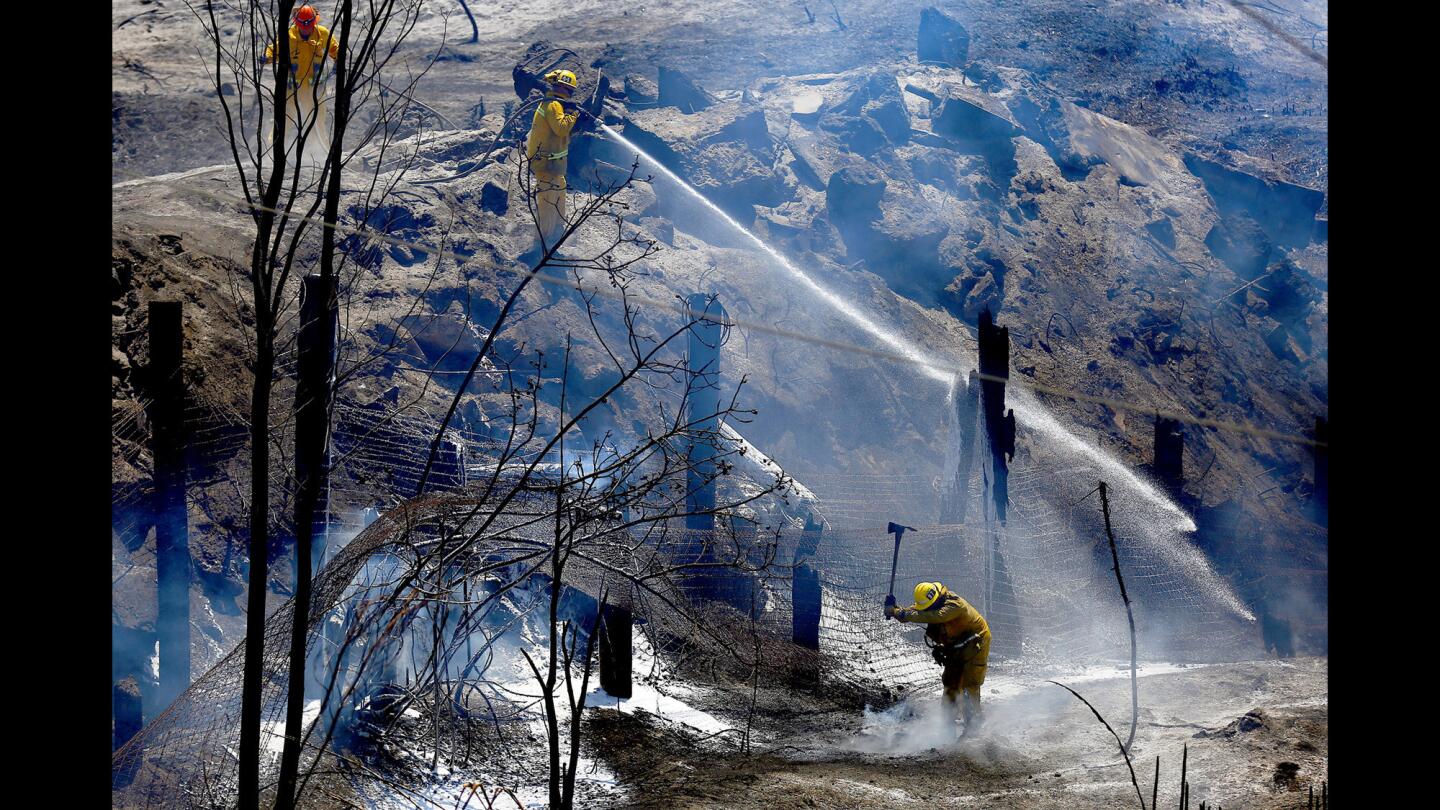 Fire Captain Dan Engraf, upper left, firefighter/paramedic Taz Waller and firefighter Eric Marrufo work to extinguish hot spots after a weekend fire that ravaged the Montebello Hills area near the Rio Hondo River. About 225 acres were burned and power lines were down in the area.