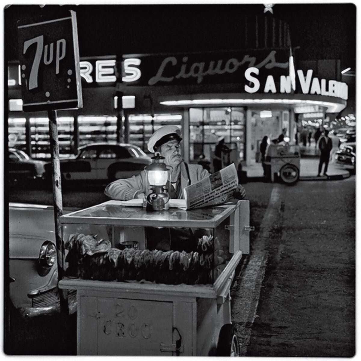 A taco vendor catches up on the news until the next customer shows up in this 1964 photograph by Harry Crosby, in the collection of Paul Ganster.
