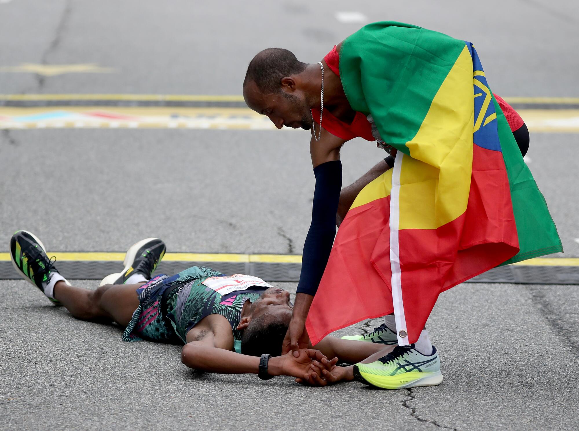 Marathon winner Jemal Yimer helps his countryman Yemane Tsegay, who collapsed after finishing second.