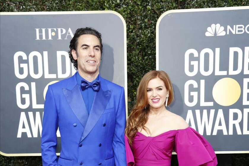 Sachan Baron Cohen in a bright blue suit holding hands and posing with Isla Fisher in a magenta gown with puff sleeves