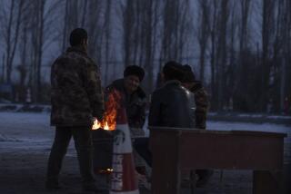 Men gather near a fire at a checkpoint into Wushi county in China's western Xinjiang region on Tuesday, Jan. 23, 2024. A massive earthquake has struck a sparsely populated part of China's western Xinjiang region, killing a few and damaging or collapsing more than 120 homes in freezing cold weather. (AP Photo/Ng Han Guan)