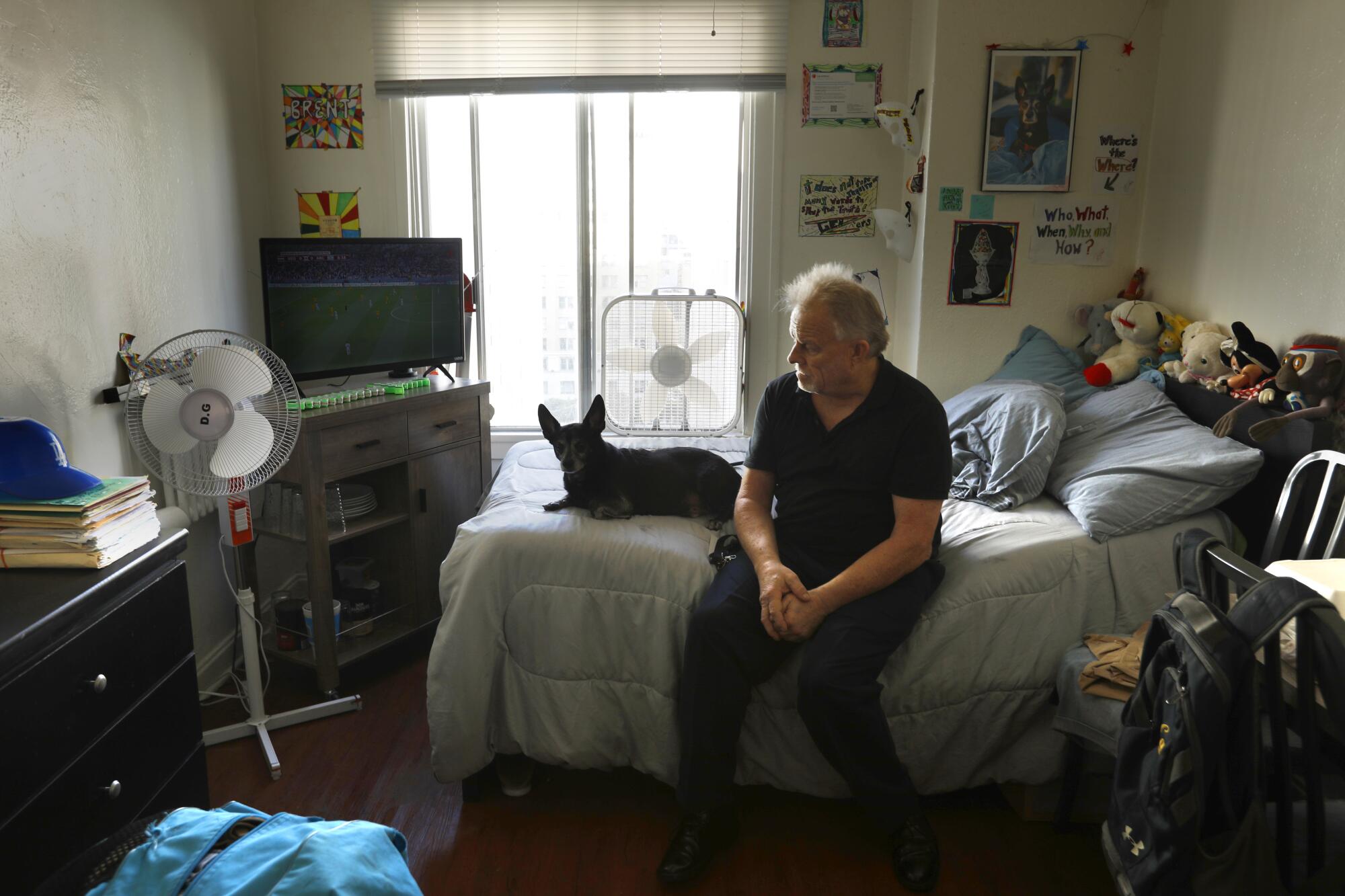 A man sits on a bed with his dog lying next to him 