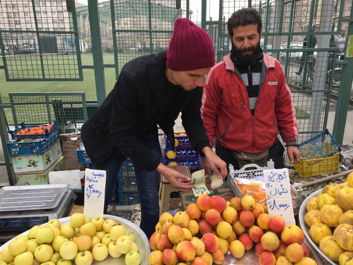 Ali Jafari, right, abandoned his factory job to sell fruits at Jomeh Bazaar, a weekly sidewalk market in middle-class western Tehran.