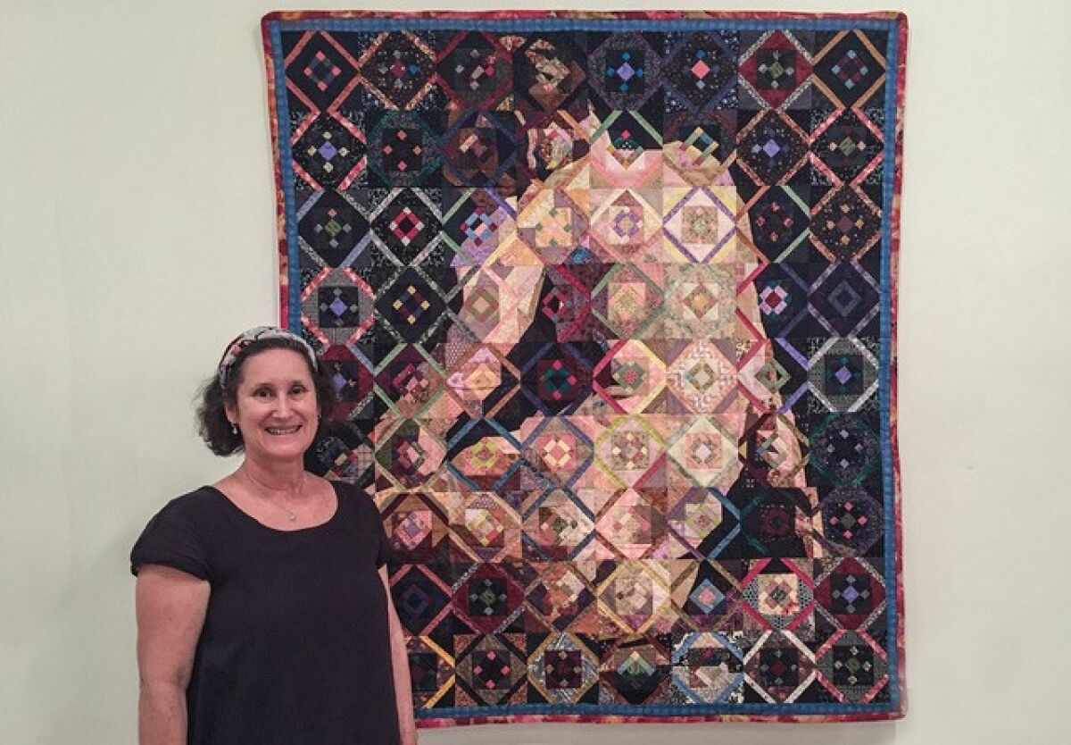 Visions’ new Executive Director Laura Mitchell with ‘Eakins Odalisque,’ a quilt by Jack Edson from Hamburg, New York, based on a photo of the late-19th-century artist Thomas Eakins posing (in classic odalisque position) for a friend.