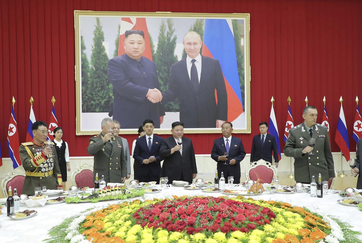 Men in suits and military uniforms stand at a table with a huge floral arrangement in the center 