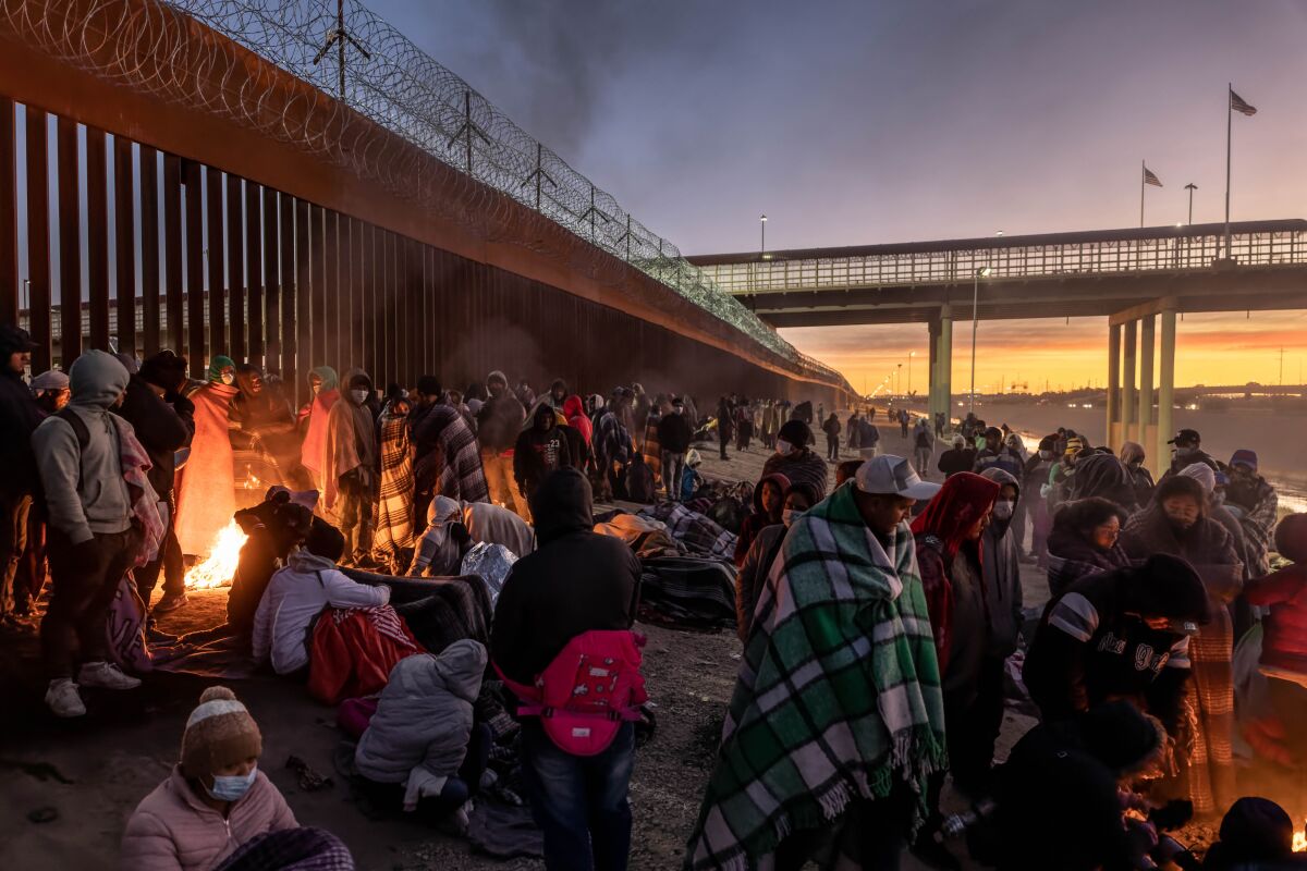 Migrants bundle up against the cold in front of a fire.
