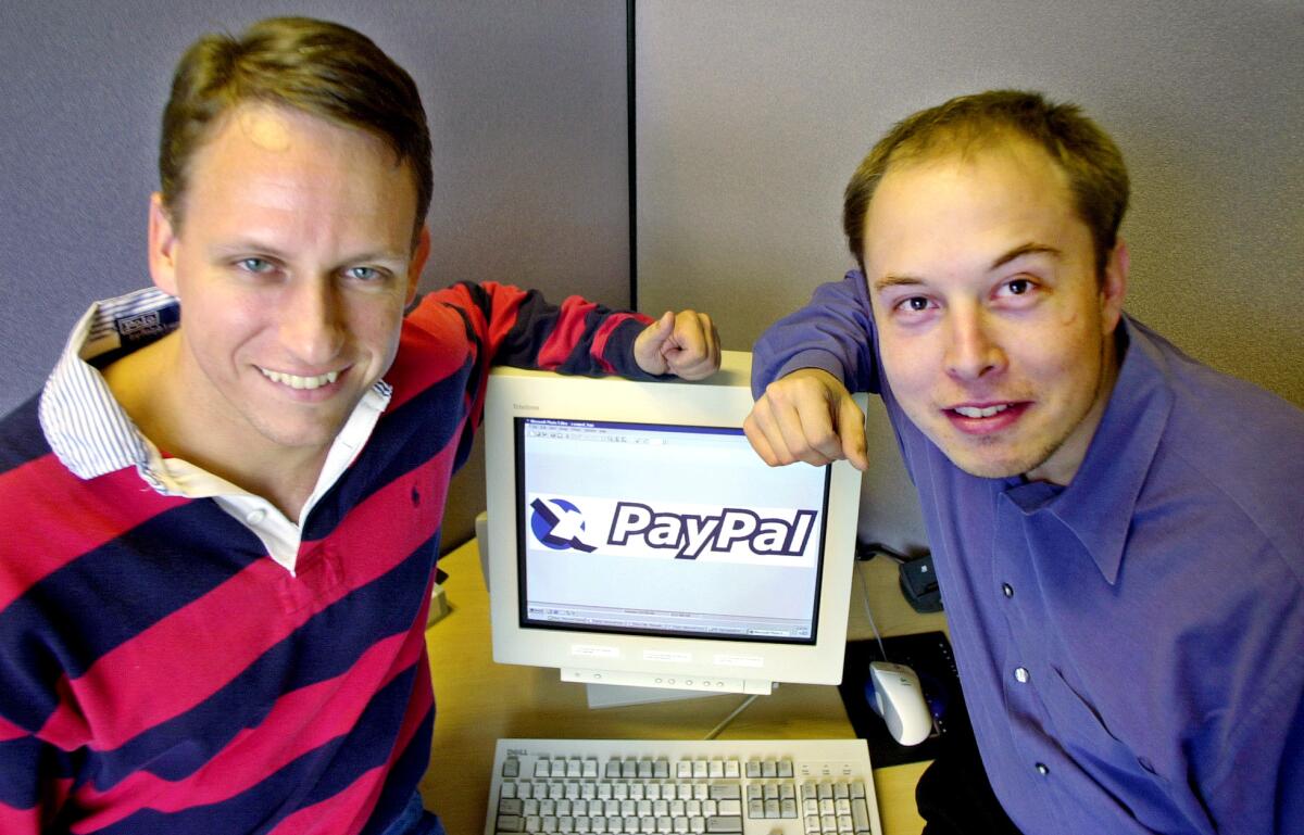 A man in a striped shirt and a man in a button-down shit both lean onto a computer monitor.