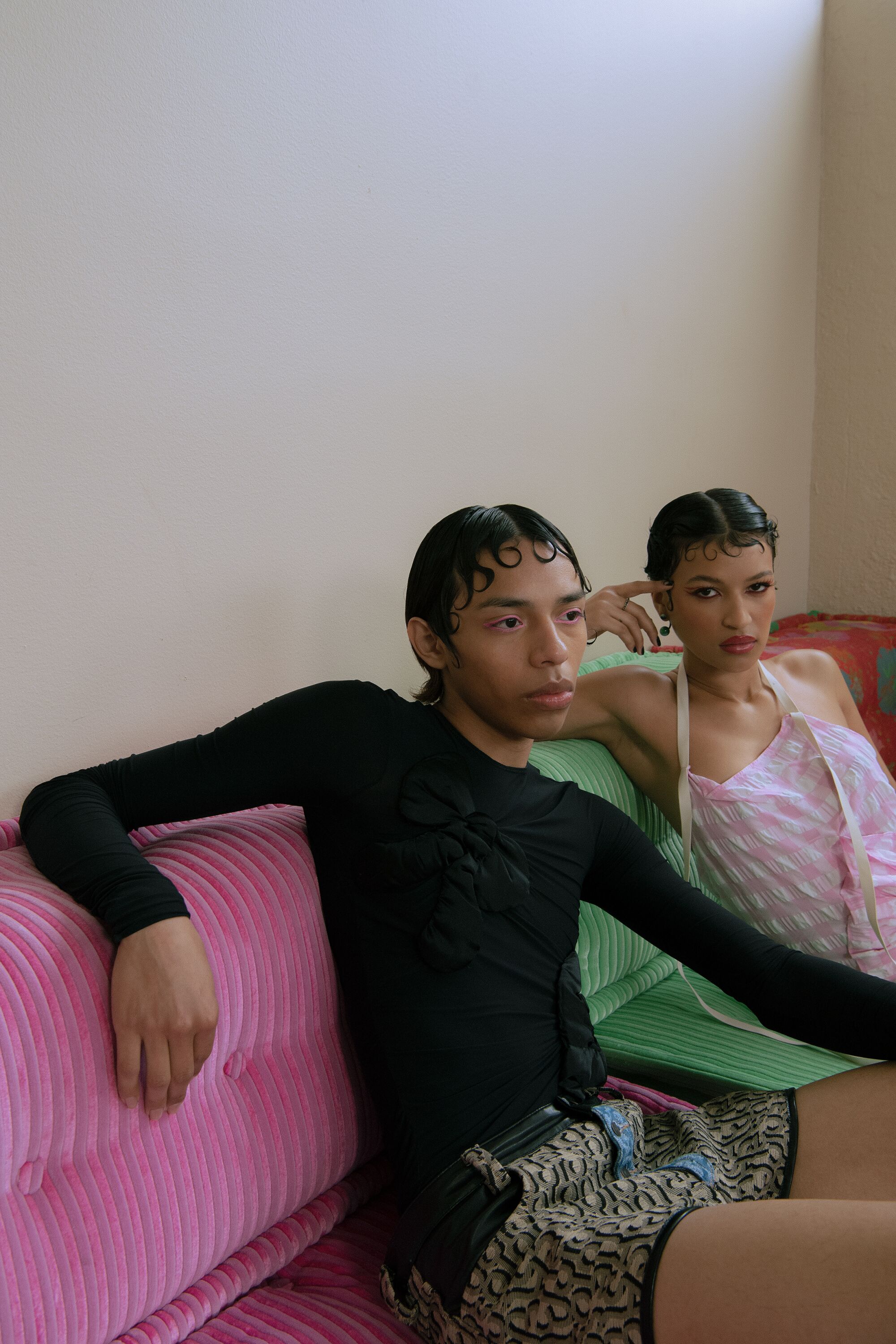 Two models lounge on a couch, one looks into the distance and the other looks at the camera.