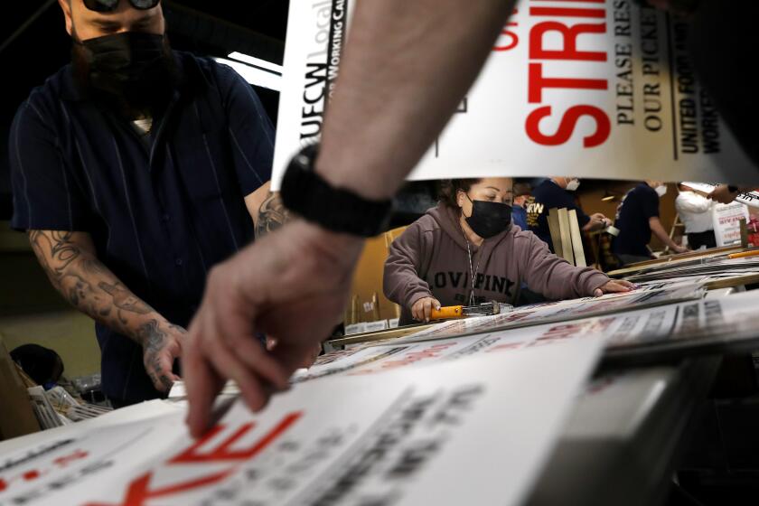 LOS ANGELES-CA-MARCH 21, 2022: Tyson Kehm, left, and Andrea Garcia, right, help make strike-ready signs at UFCW Local 770 headquarters in Los Angeles on Monday, March 21, 2022. (Christina House / Los Angeles Times)