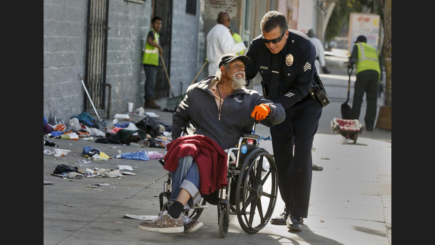 LAPD Sgt. Jack Richter helps a homeless man in a wheelchair leave an area along 5th Street as the cleanup of skid row continues with city sanitation crews sweeping and later power washing the sidewalks.