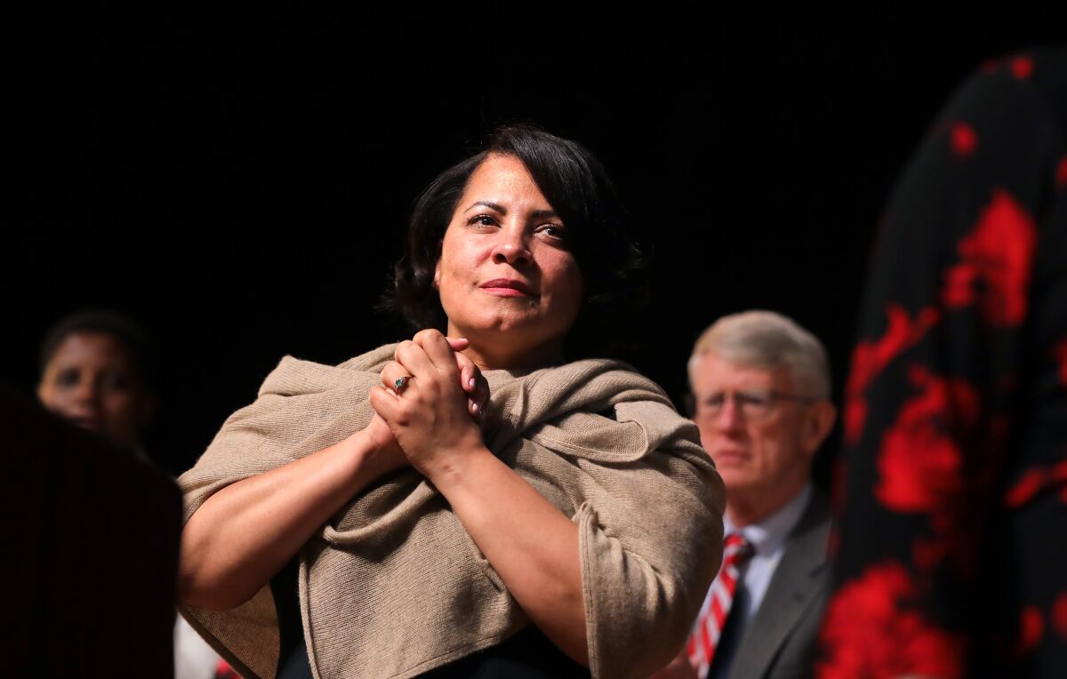 A woman clasps her hands under her chin.