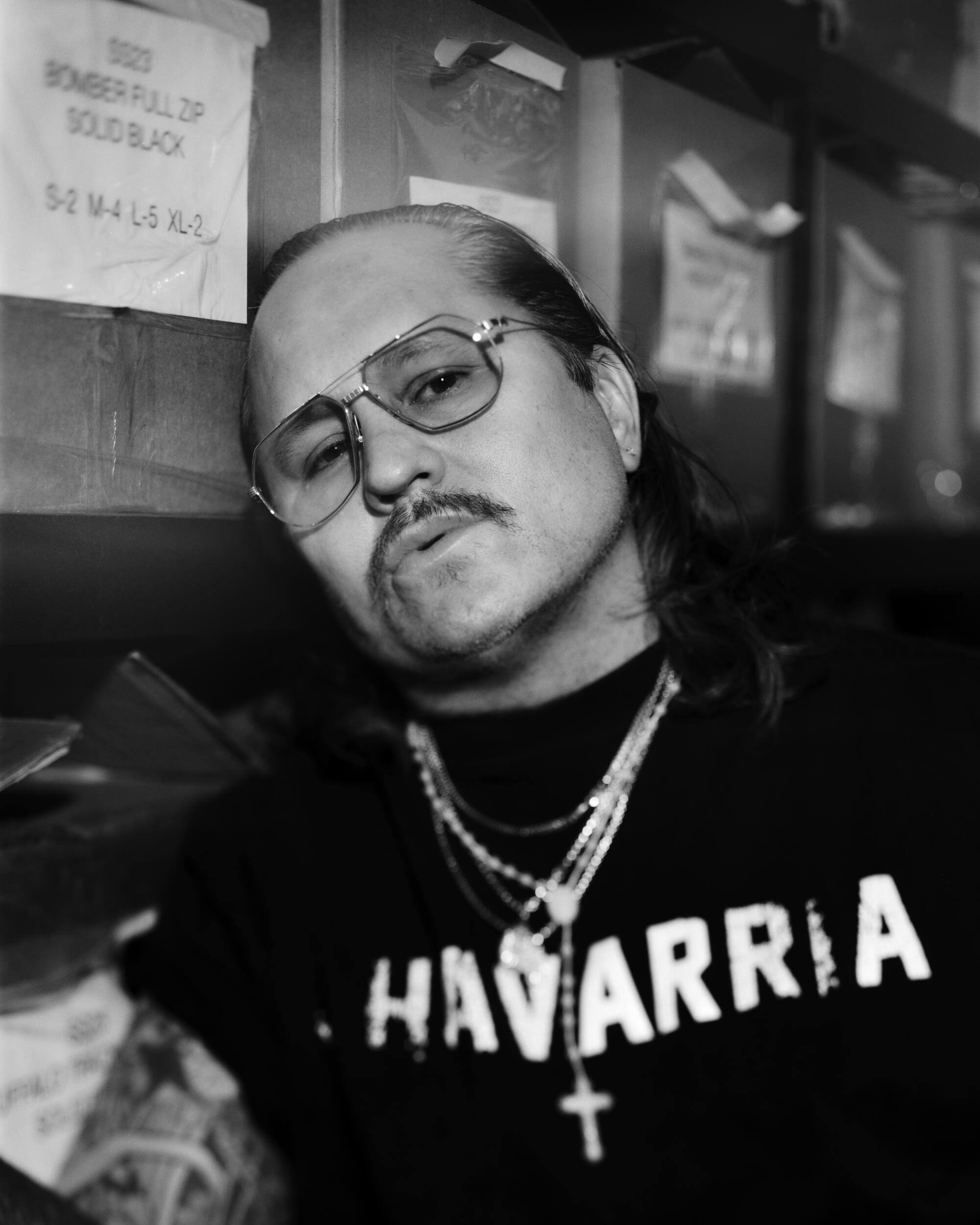 A man in a dark T-shirt with the word Chavarria on it, wearing several necklaces
