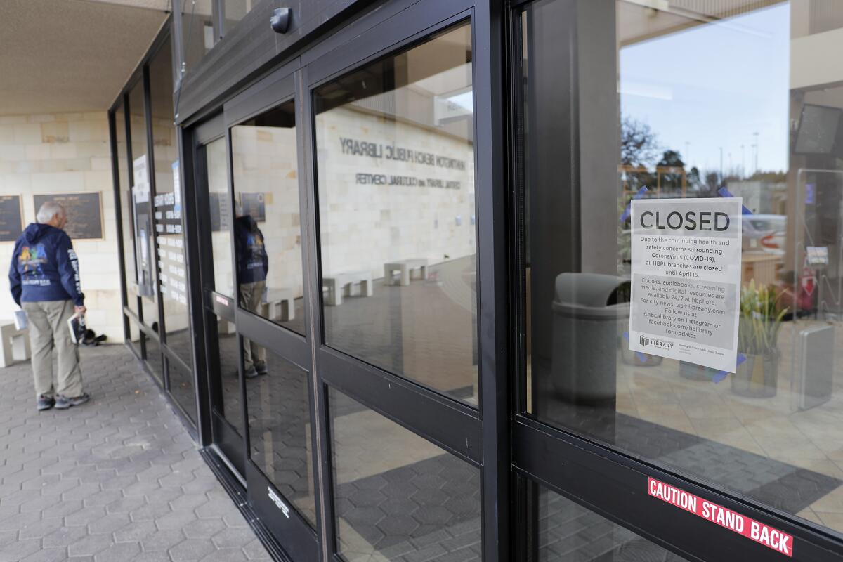 A patron reads a notice Tuesday on the book-return window at Huntington Beach Central Library to "Keep your books." All Huntington Beach Library branches are closed to the public through April 15 due to safety concerns over the coronavirus. Late fines, fees and holds are suspended during that time.