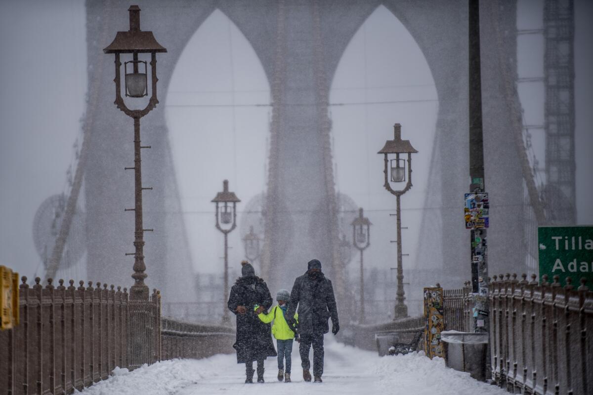 ARCHIVO - Dos adultos y un niño cruzan el puente de Brooklyn durante una tormenta de nieve